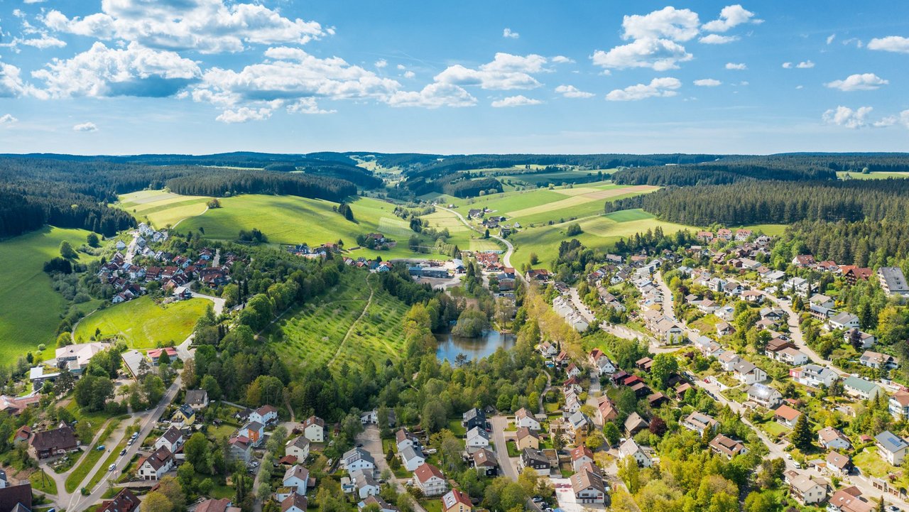 Luftbild Unterkirnach mit Ortsmitte, grüner Wiese und blaumen Himmel